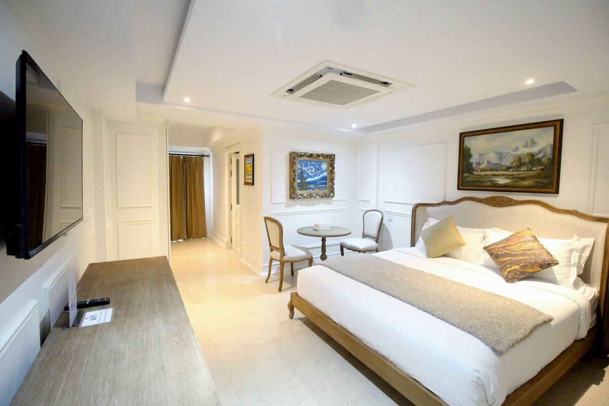 A hotel room with a large bed, a desk, a chair, and a television.