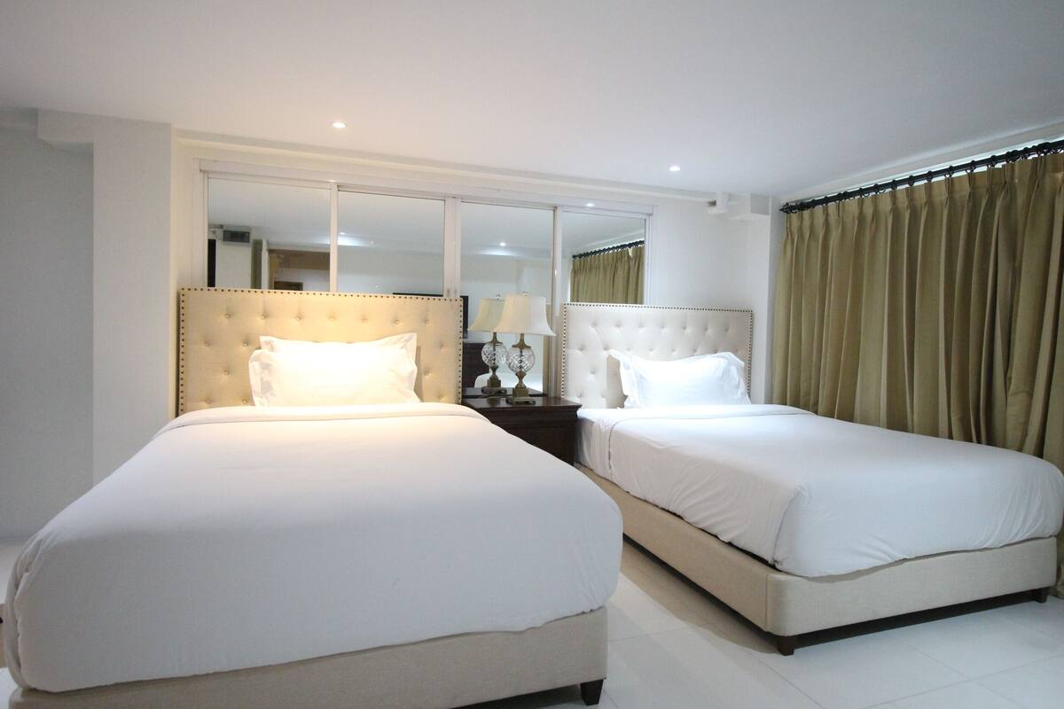 A hotel room with two beds, a large mirror, and a window with curtains.