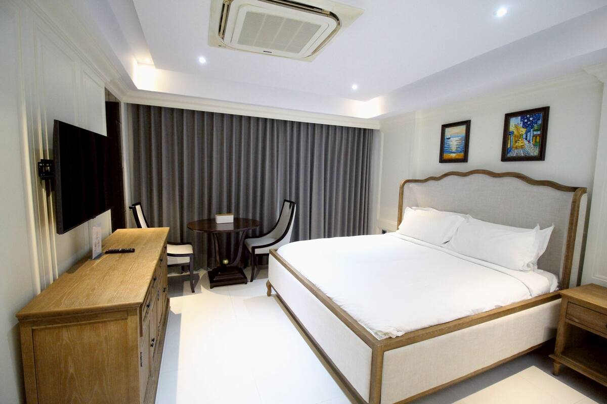 A hotel room with a large bed, a desk with a chair, a television, and two paintings on the wall.