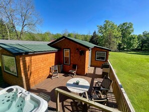 Una cabaña de madera con terraza, jacuzzi y mobiliario exterior.