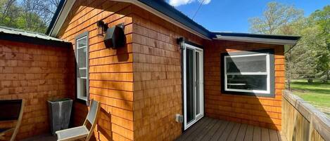 A wooden cabin with a deck, a sliding glass door, and a window.