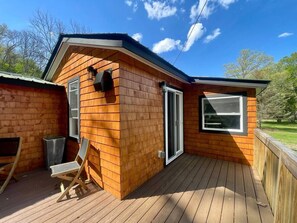 Une cabane en bois dotée d’une terrasse, d’une porte-fenêtre coulissante et d’une fenêtre.