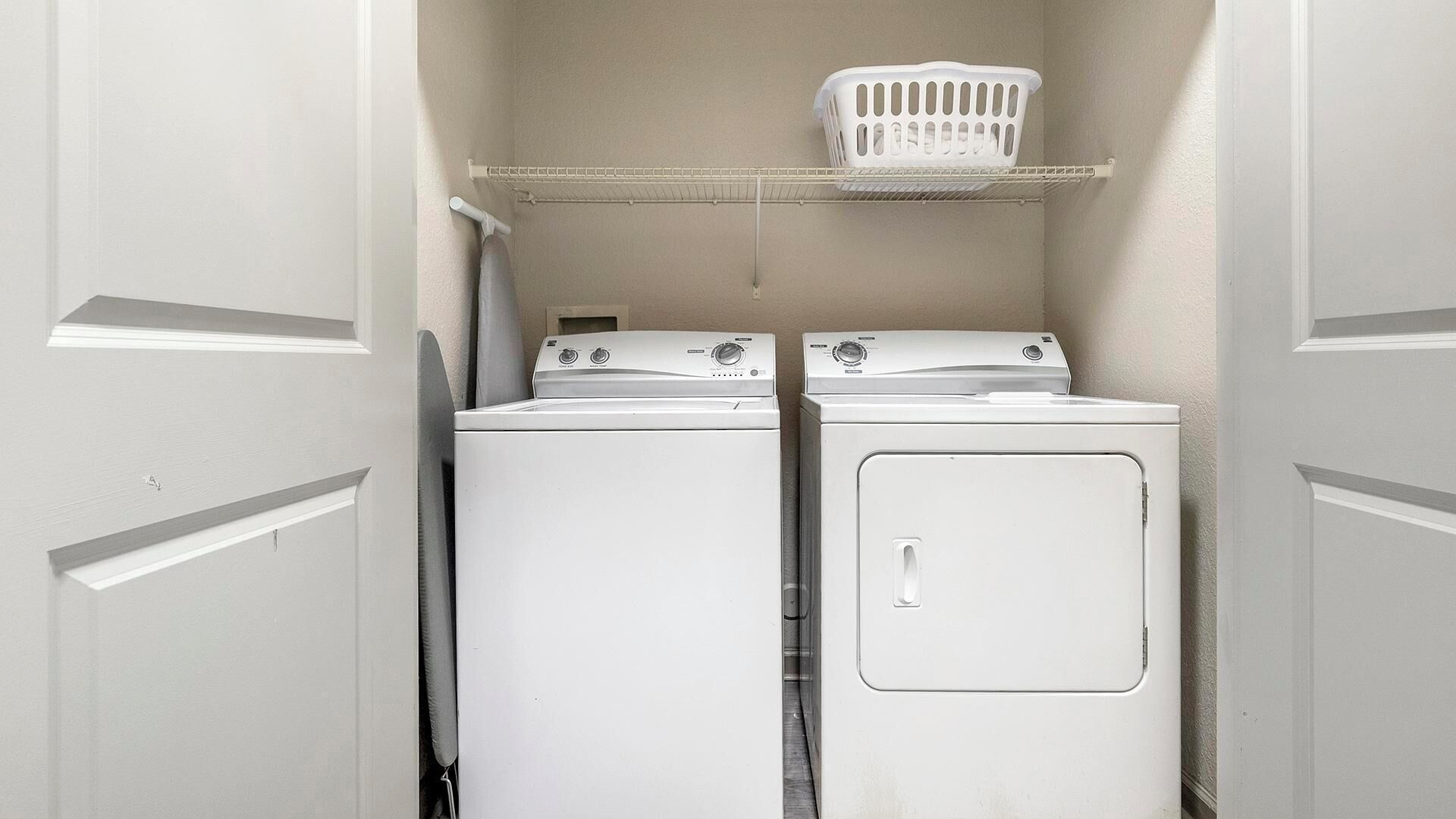 A laundry room with two stacked washers and dryers, a white laundry basket on a shelf, and a towel hanging on the wall.