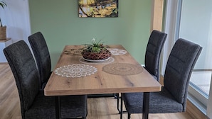 Una mesa de comedor con cuatro sillas, un centro de mesa con planta y un cuadro de un bosque en la pared.