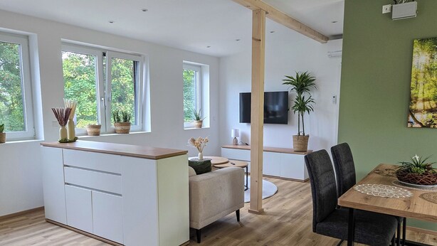 Una cocina moderna con una isla central, zona de comedor con mesa y sillas, y un televisor montado en la pared.