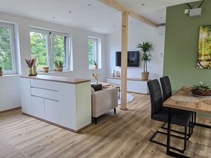 Une cuisine moderne dotée d’un îlot central, d’un coin repas avec une table et des chaises, et d’un téléviseur fixé au mur.