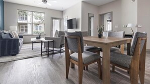 A modern living room with a dining area, large windows, and a flat-screen TV.