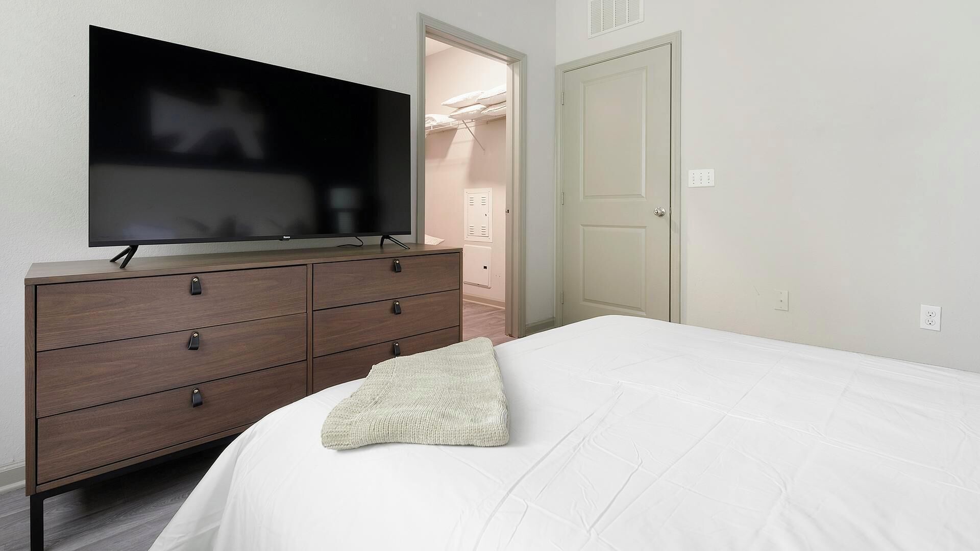 Une chambre à coucher avec un lit, une commode sur laquelle se trouve un téléviseur et un placard rempli de vêtements.