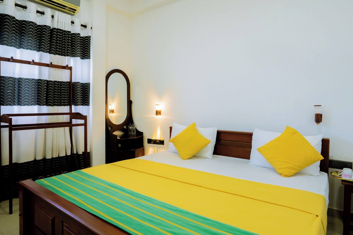 A hotel room with a bed, a nightstand, a mirror, and a wall-mounted light.