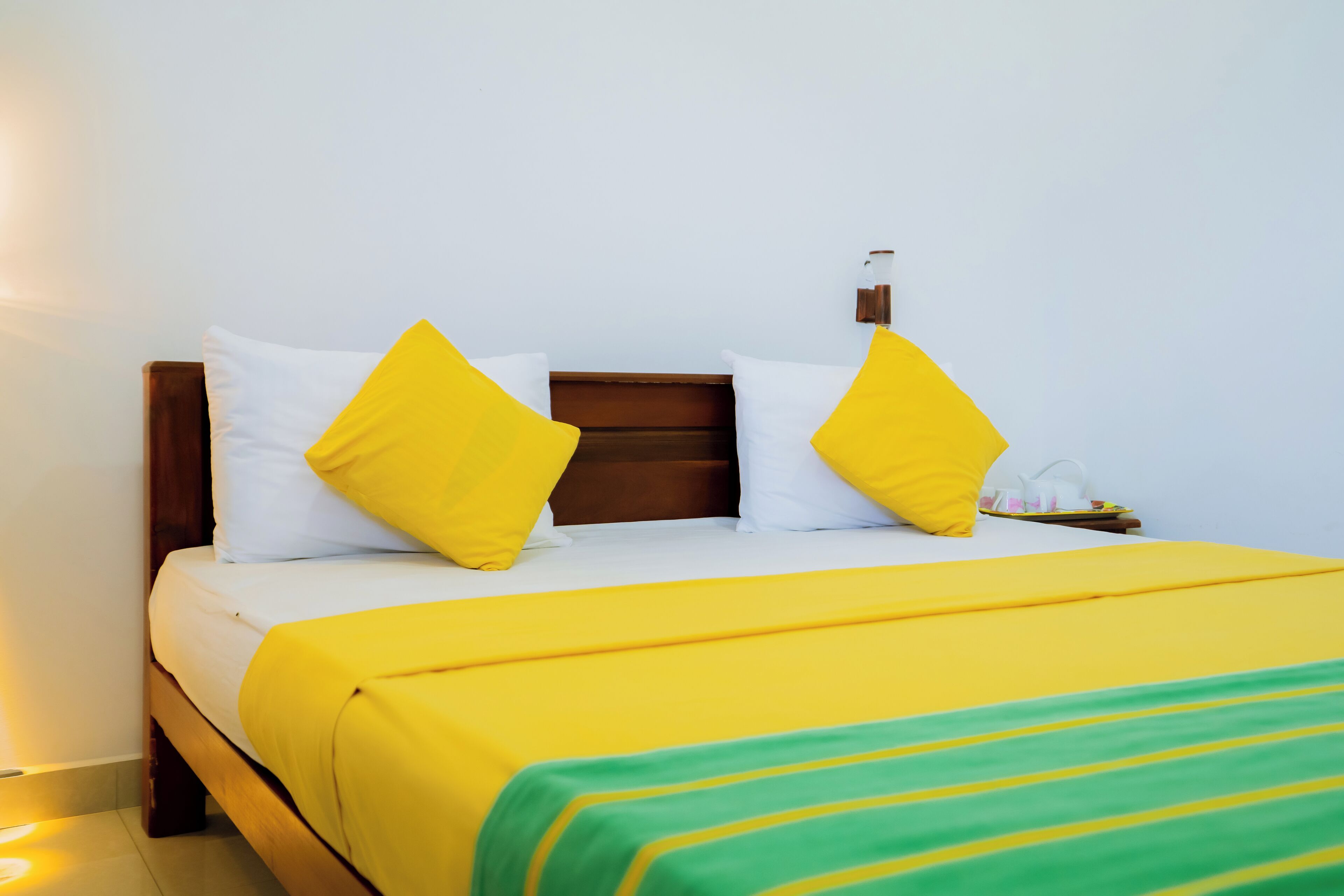 A neatly made bed with yellow and white bedding, a wooden headboard, and a bedside table with a lamp.