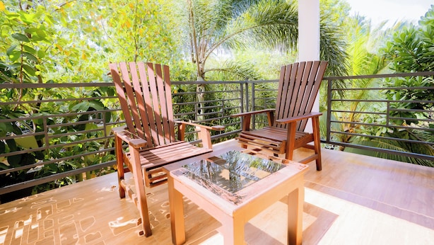 A wooden deck with two chairs and a table, surrounded by lush greenery and a metal railing. - Blue Sky Hotel Yala (Mahasenpura)
