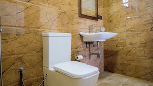 A bathroom with a marble wall, a toilet, a sink, and a mirror. - Blue Sky Hotel Yala (Mahasenpura)