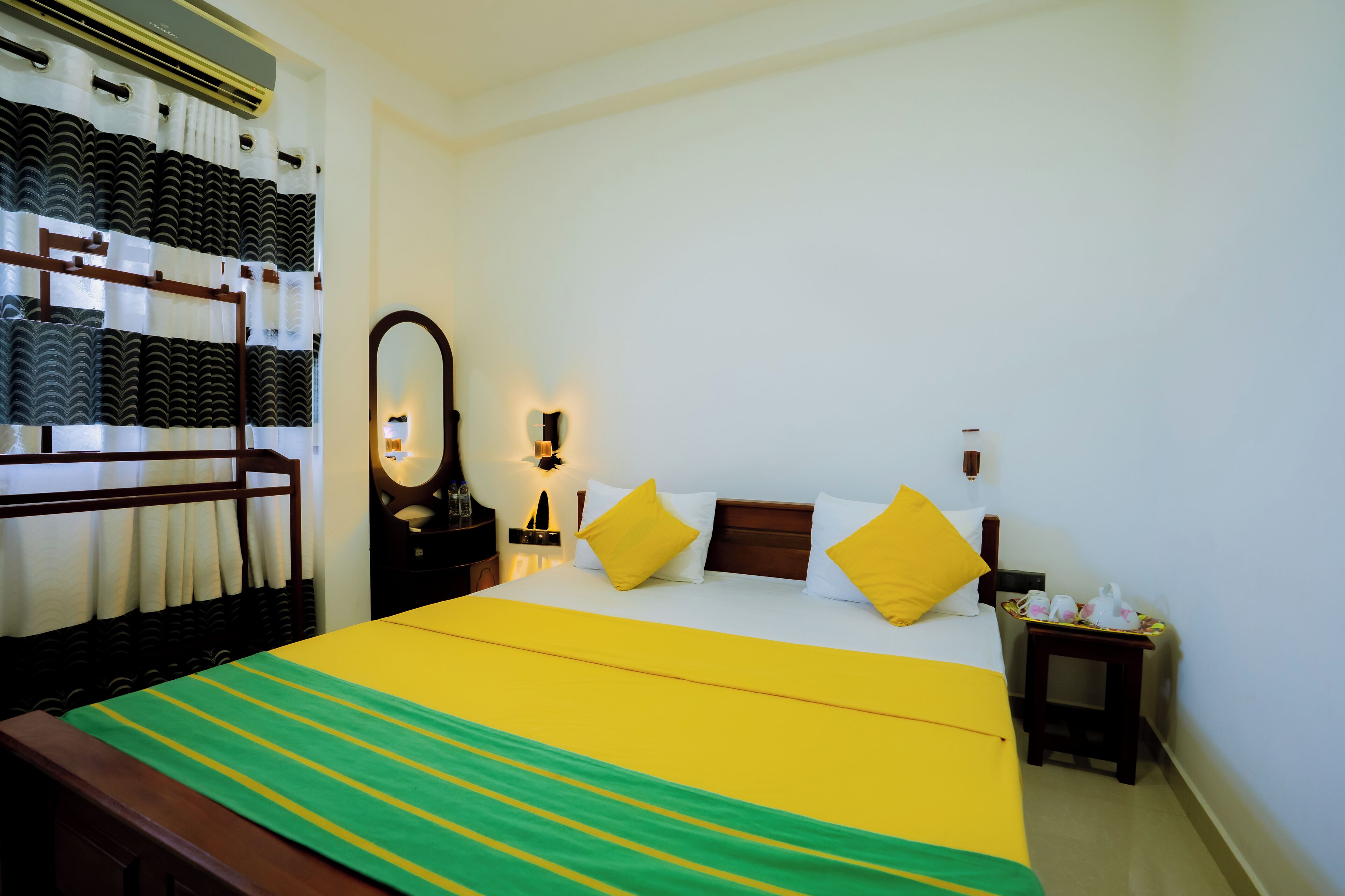 Habitación de hotel con cama, mesita de noche, espejo y aire acondicionado de pared.