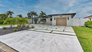 Een modern huis met een oprit van beton, palmbomen en een verzorgd gazon.