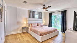 A bedroom with a bed, bedside lamps, a ceiling fan, and a view of the outdoors. - Parrots Cove (St. Pete Beach)