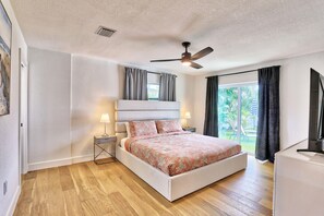 A bedroom with a bed, bedside lamps, a ceiling fan, and a view of the outdoors.