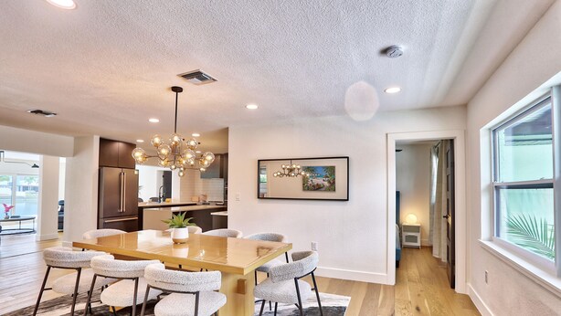 A modern dining area with a wooden table, six chairs, and a chandelier. - Parrots Cove (St. Pete Beach)