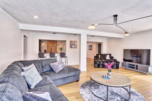 A modern living room with a grey sectional sofa, a round coffee table, and a TV in the background. - Parrots Cove (St. Pete Beach)