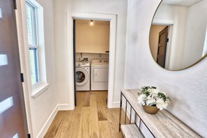 A hallway leading to a laundry area with a wooden floor and a mirror on the wall.