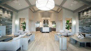 A spacious lobby with a central reception desk, two seating areas with sofas and coffee tables, and a modern chandelier.