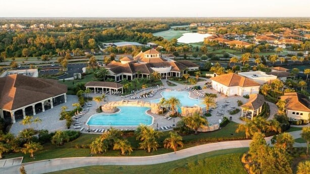 A resort with a central swimming pool, multiple guest villas, and a golf course in the background.
