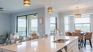A modern kitchen with a large island, pendant lights, and a view of the outdoors.
