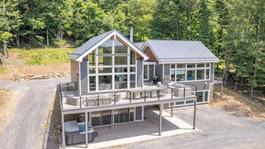 A modern two-story house with large windows, a balcony, and a covered outdoor area. - Gorgeous Lake Retreat w/ Hot Tub & Pool! (McHenry)