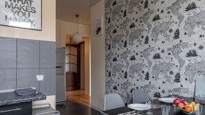 A modern dining area with a black and white patterned wallpaper, a white pendant light, and a table set for two with plates, glasses, and a fruit bowl. - Family apartments near Gorky Park (Minsk)