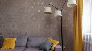 A modern living room with a sectional sofa, patterned wallpaper, a floor lamp, and a window with yellow curtains. - Family apartments near Gorky Park (Minsk)