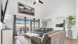 A modern living room with a leather sofa, a flat-screen TV mounted on the wall, and a large window with curtains. - Private Pool! 3-Min To The Beach (Noord)