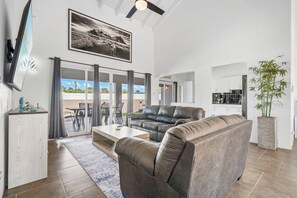 Ett modernt vardagsrum med en lädersoffa, en platt-TV som är monterad på väggen och ett stort fönster med gardiner.