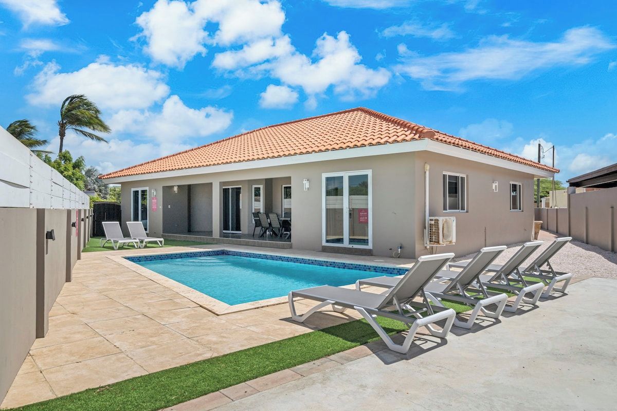 A modern building with a swimming pool, lounge chairs, and a covered patio area.