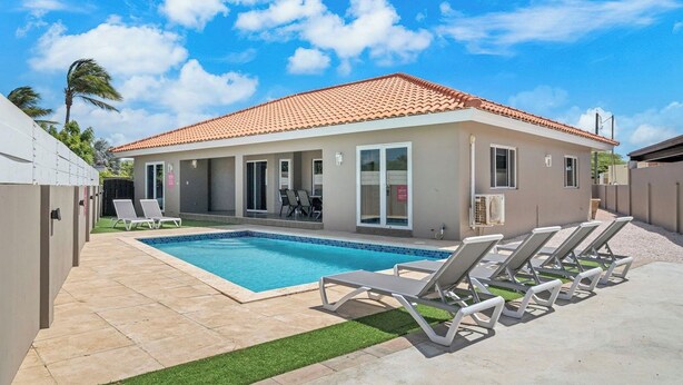 A modern building with a swimming pool, lounge chairs, and a covered patio area. - Private Pool! 3-Min To The Beach (Noord)