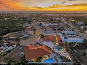 A residential area with houses, a swimming pool, and a beach in the background.