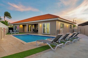 A modern house with a swimming pool, outdoor seating, and a well-maintained lawn.
