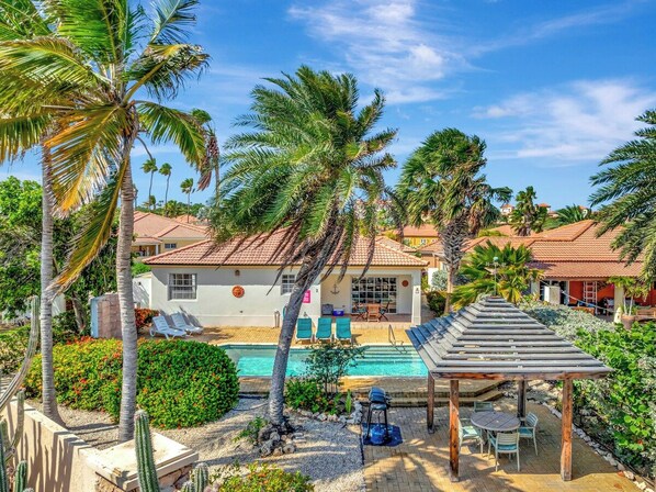 A residential property with a swimming pool, palm trees, and a covered patio area.