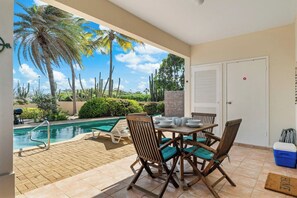 A patio with a pool, dining table, chairs, and a door.