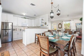 A modern kitchen with white cabinets, a stainless steel refrigerator, and a dining area with wooden chairs and a table set for four.