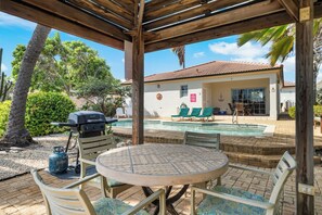 An outdoor patio with a round table and chairs, a barbecue grill, and a pool area with lounge chairs.