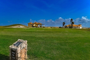 Un campo de golf con club house, bar de aperitivos y un cielo azul despejado.
