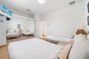 Une chambre d’hôtel avec un grand lit, deux petits lits, un téléviseur fixé au mur et une porte donnant sur une autre pièce.