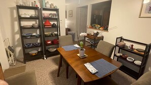 Un coin repas avec une table en bois, des chaises et une bibliothèque remplie de vaisselle et d’ustensiles de cuisine.