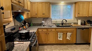 Une cuisine avec des meubles de rangement en bois, une cuisinière, un évier et une fenêtre avec des stores.