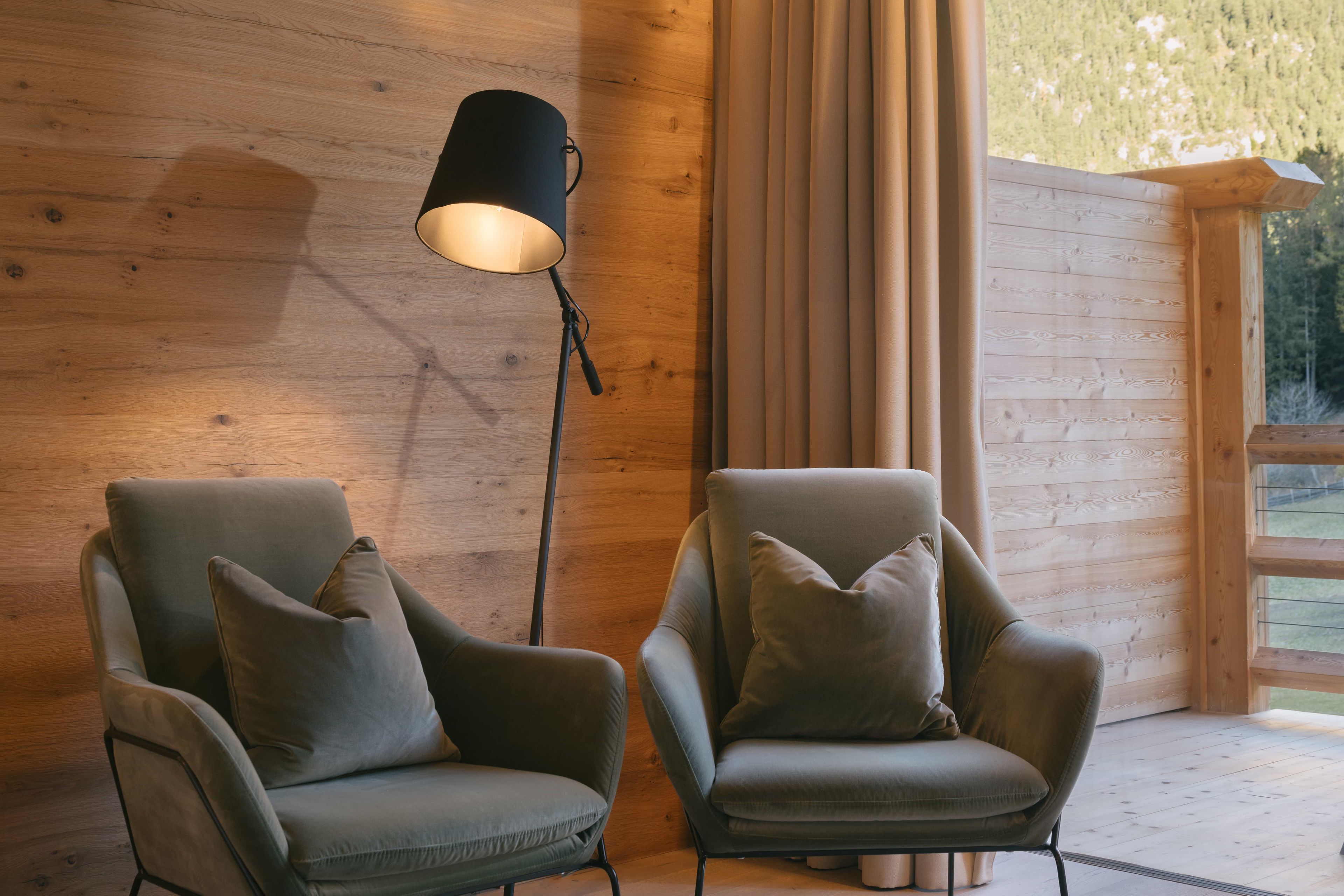 Dos sillones con cojines, una lámpara de pie y una pared de madera con un ventanal.