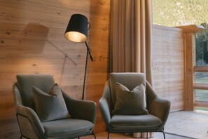 Dos sillones con cojines, una lámpara de pie y una pared de madera con un ventanal.
