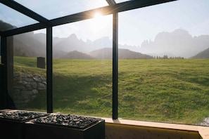 Una habitación con un ventanal grande que da a un campo cubierto de hierba y montañas.