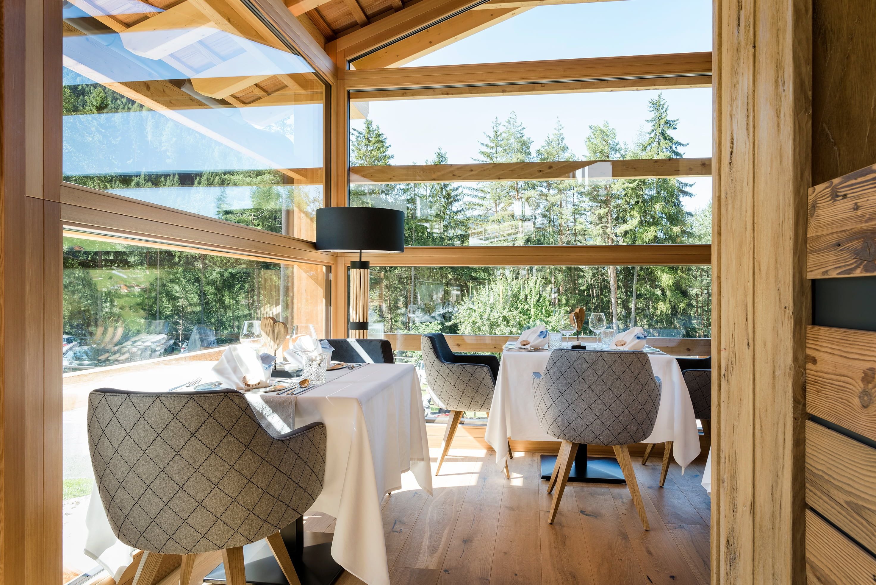 Un espace de restauration intérieur agrémenté de poutres en bois, de grandes fenêtres et de tables dressées pour le repas.