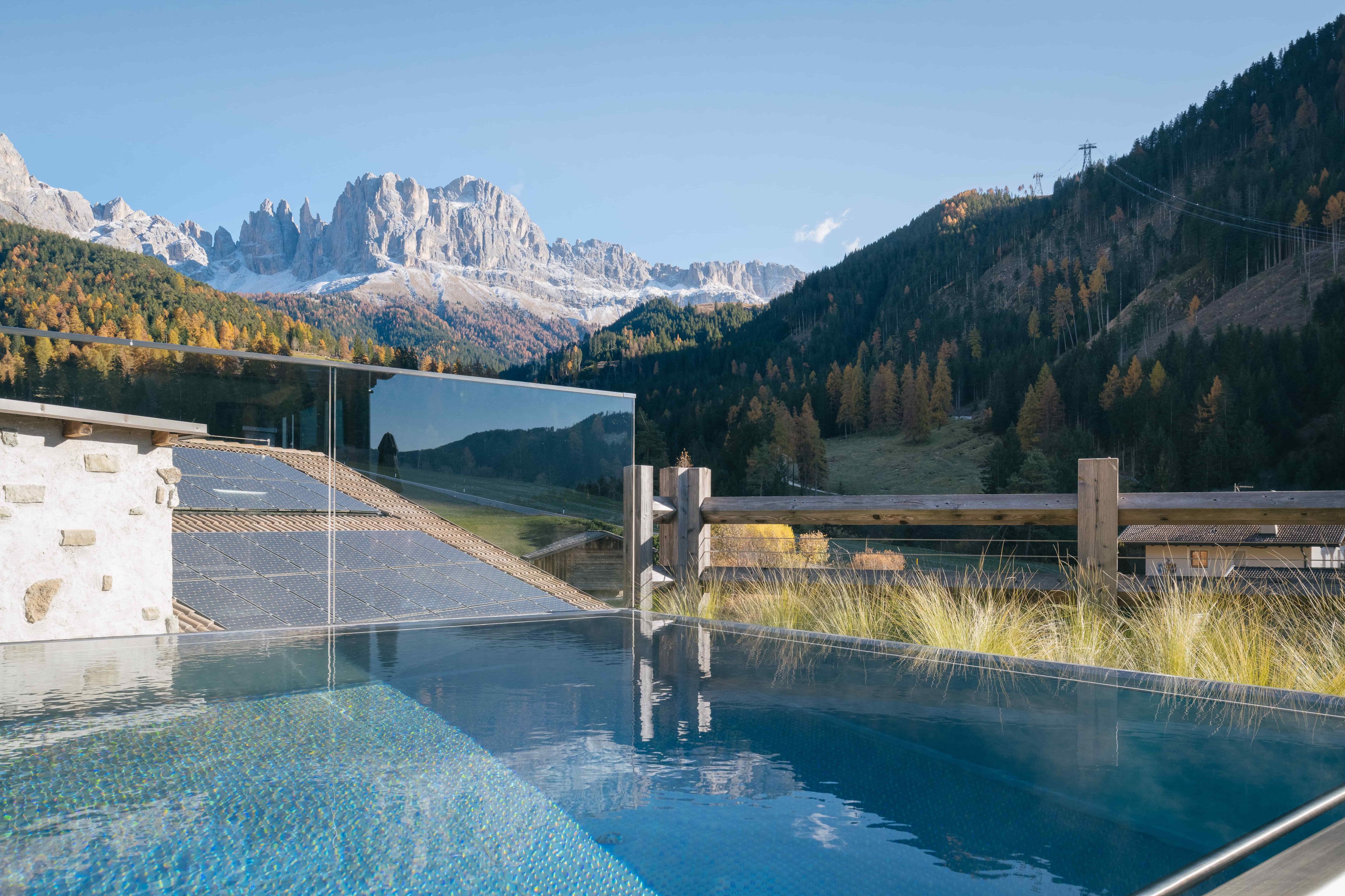 A swimming pool with a mountain backdrop, solar panels, and a wooden fence.