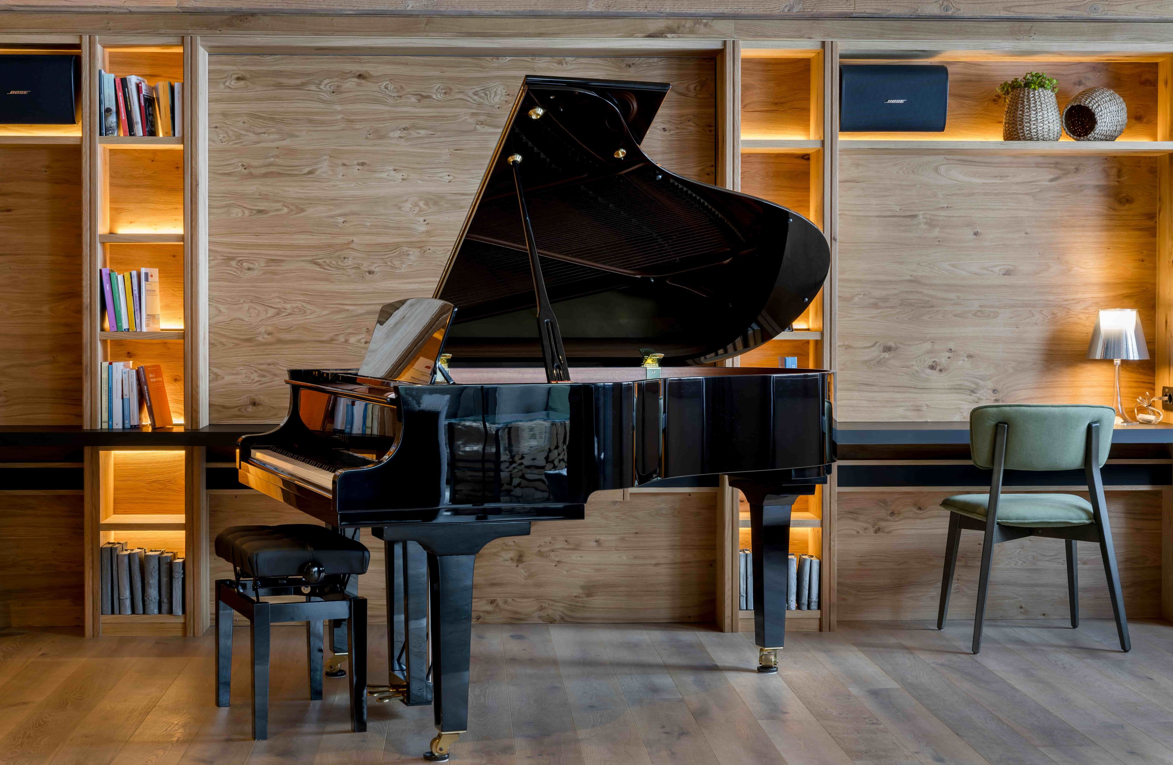 A grand piano in a room with wooden walls, bookshelves, and a chair.