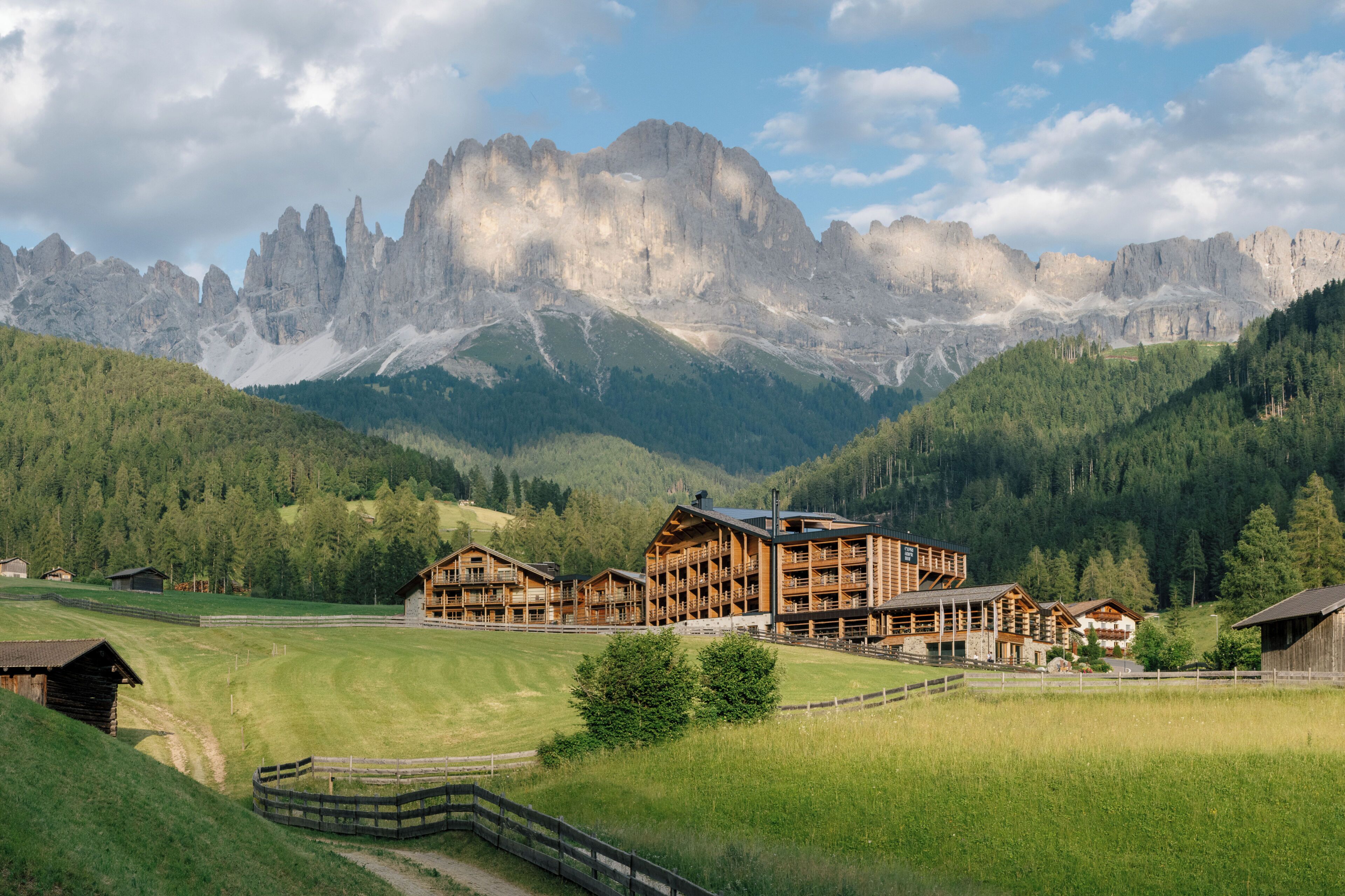 Un albergue de montaña con varias construcciones de madera, rodeado de exuberante vegetación y montañas escarpadas al fondo.